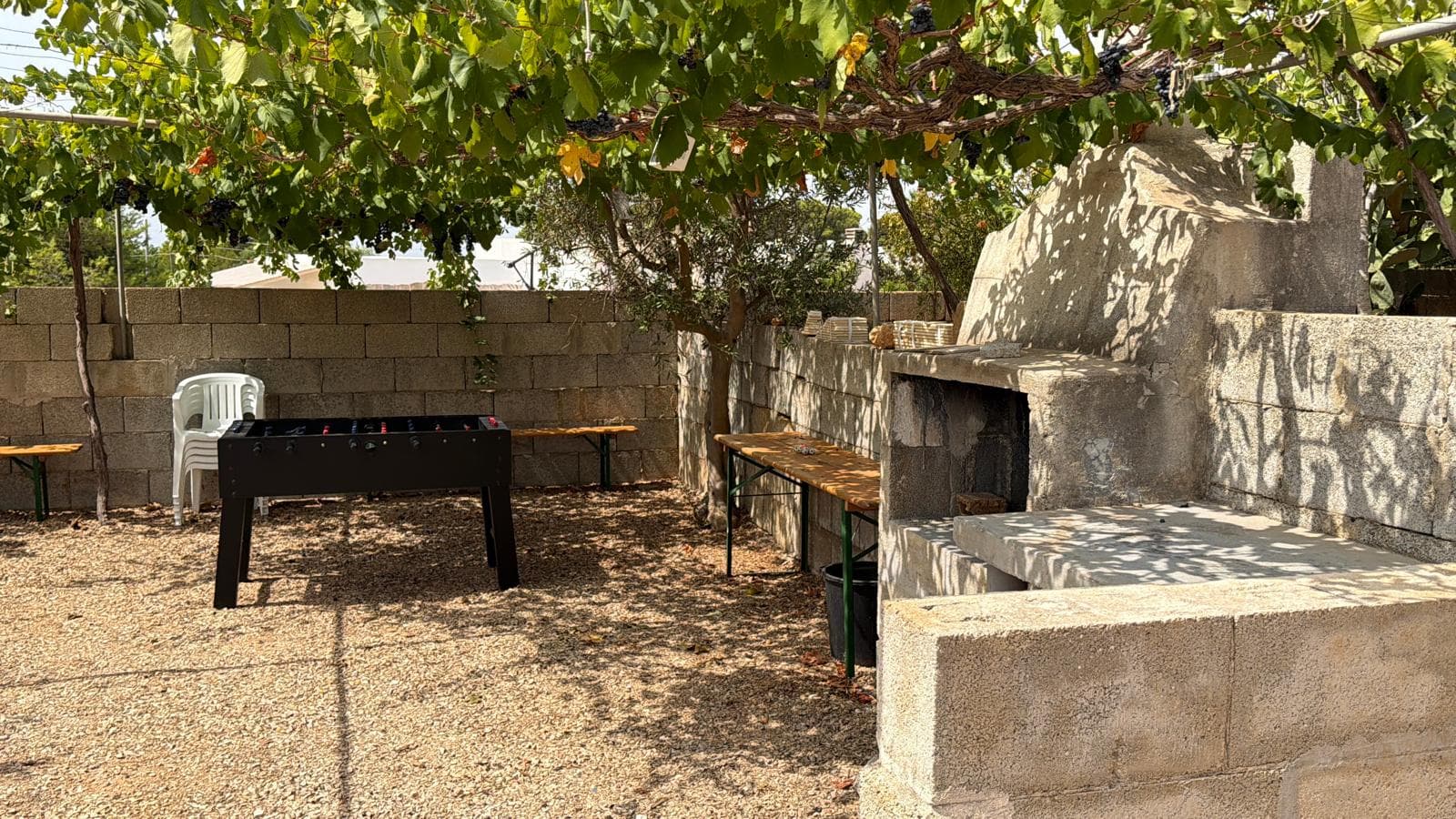 Il barbecue in pietra sotto il pergolato d'uva, con biliardino e tavoli